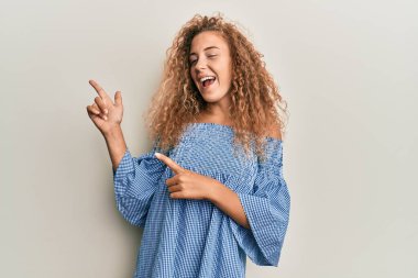 Yazlık elbise giyen güzel beyaz kız gülümseyip kameraya bakıyor ve iki eliyle ve parmaklarıyla kenarı işaret ediyor.. 