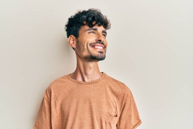 Gündelik kıyafetler giyen genç İspanyol bir adam yüzünde gülümsemeyle yan yana bakıyor, doğal bir ifade. Kendinden emin gülen. 