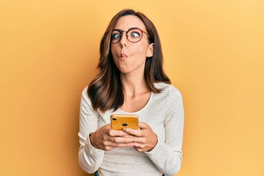 Genç esmer kadın sarı arka plan üzerinde akıllı telefon kullanıyor. Ağzı ve şaşı gözleriyle balık suratı yapıyor. Deli ve komik.. 