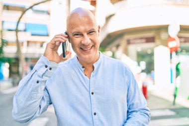 Orta yaşlı kel adam gülümsüyor. Şehirdeki akıllı telefondan mutlu mesut konuşuyor..