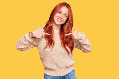 Kış süveteri giyen genç, kızıl saçlı bir kadın. Kendine güvenen, gülümseyen, kendini gururlu ve mutlu gösteren bir kadın.. 