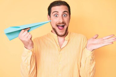 Elinde kağıt uçak tutan genç yakışıklı adam başarıyı mutlu bir gülümsemeyle ve kazanan yüz ifadesiyle kutluyor. 