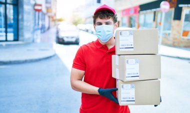 Coronavirus koruması takan beyaz bir kurye elinde karton paketler, şehirde yürüyor..