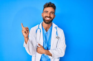 Doktor üniforması ve steteskop giyen genç İspanyol adam gülümsüyor. 