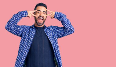 Gündelik kıyafetler giyen genç İspanyol adam barış sembolü yapıyor. Yüzünde parmaklar, gülümseyerek zaferi gösteriyor. 