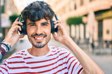 Mutlu gülümseyen ve kulaklık takan genç İspanyol adam şehrin caddesinde yürüyor..