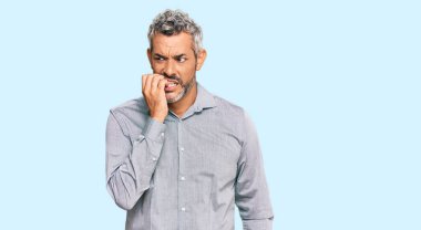 Orta yaşlı, gri saçlı, günlük kıyafetler giyen, gergin ve elleri ağızda olan, tırnaklarını yiyen bir adam. anksiyete. 