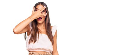 Günlük kıyafetler ve gözlük takan genç İspanyol kadın şok içinde yüzünü ve gözlerini kapayarak utangaç ifadesiyle parmaklarından bakıyor.. 