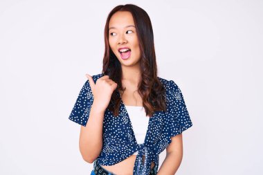 Genç, güzel Çinli bir kız, günlük kıyafetler giyiyor, gülümsüyor, gülümsüyor ve başparmağıyla yan tarafı işaret ediyor.. 