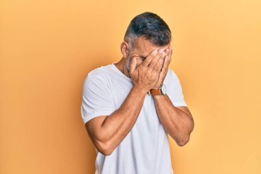 Orta yaşlı yakışıklı bir adam, günlük beyaz tişörtler giyiyor ve ağlarken suratını ellerle kapatıyor. depresyon kavramı. 