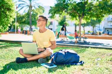 Üniversite kampüsünde çimlerin üzerinde otururken mutlu bir şekilde gülümseyen İspanyol öğrenci.