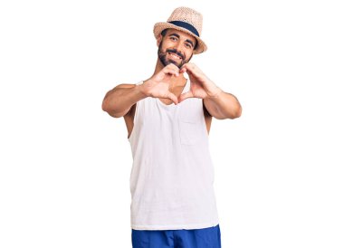 Gündelik yaz şapkası takan, aşık gülümseyen, elleriyle kalp sembolü yapan genç İspanyol bir adam. romantik kavram. 