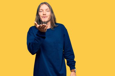 Uzun saçlı yakışıklı beyaz adam, sıradan bir kazak giyiyor kameraya bakıyor ve havada el ele öpüşüp güzel ve seksi oluyor. aşk ifadesi. 