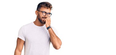 Günlük kıyafetler ve gözlük takan genç İspanyol adam gergin ve gergin görünüyor. Elleri ağızda, tırnaklarını yiyor. anksiyete. 