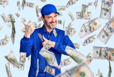 Orta yaşlı, tamirci üniforması giyen yakışıklı bir adam arka tarafı işaret ediyor.