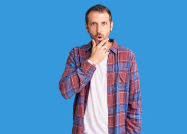 Gündelik giysiler giyen genç yakışıklı adam, elleri çenesinde, inanılmazlık, şaşkınlık ve şaşkınlık dolu bir ifade takınıyor. 