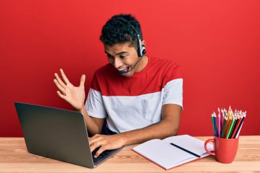 Ofiste çalışan yakışıklı Afrikalı Amerikalı genç adam operatör kulaklığı takıyor zaferi mutlu bir gülümsemeyle kutluyor ve kazanan ifade ellerini kaldırıyor. 