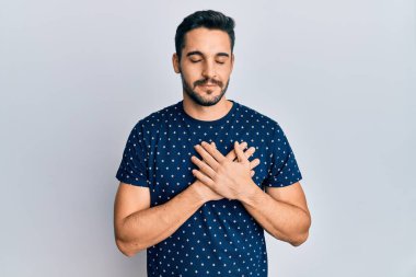 Gündelik kıyafetler giyen genç İspanyol adam elleri göğsünde gülümsüyor, gözleri kapalı ve yüzünde minnet ifadesi var. sağlık kavramı. 