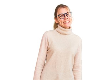 Balıkçı yaka kazak giyen, gözlüklü, yüzünde gülümseme, doğal bir ifade olan genç, güzel sarışın kadın. Kendinden emin gülen. 