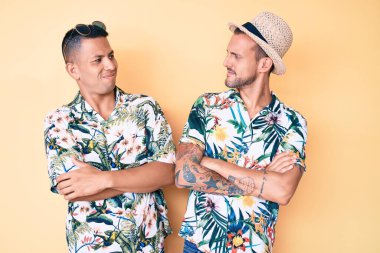 Yazlık şapkalı ve Hawaii gömlekli iki genç eşcinsel kolları çapraz ve kendinden emin bir şekilde yan tarafa bakıyor. 