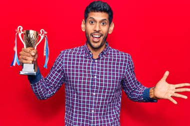 Kazanan kupayı elinde tutan genç latin adam zaferi mutlu bir gülümsemeyle ve kazanan yüz ifadesiyle kutluyor. 