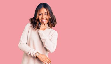 Balıkçı yaka kazak giyen genç ve güzel bir kadın kameraya kendinden emin bakıyor kollarını kavuşturmuş ve çenesini kaldırmış gülümsüyor. Olumlu düşünmek. 