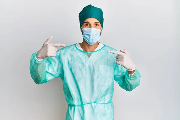 Fiatal Jóképű Férfi Sebész Egyenruhában Orvosi Maszkban Vidám Mosollyal Mutogatva — Stock Fotó
