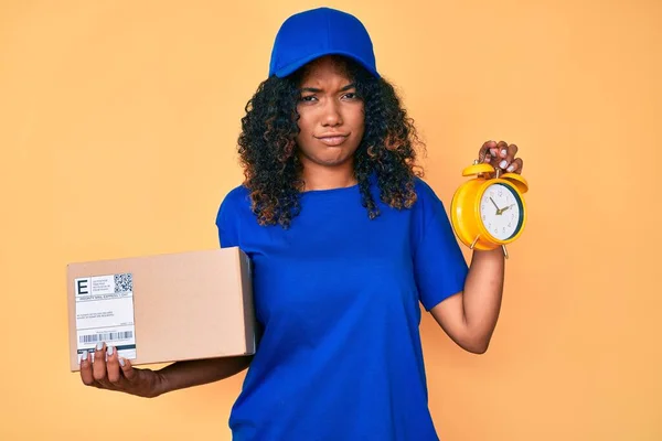 配達パッケージと目覚まし時計の懐疑的で神経を保持している若いアフリカ系アメリカ人女性は 問題のために動揺を眉をひそめています 否定的な人 — ストック写真
