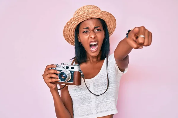 Young african american woman wearing summer hat holding vintage camera pointing displeased and frustrated to the camera, angry and furious with you