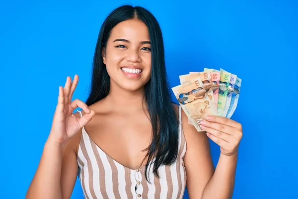 Mladá Asijská Dívka Drží Kanadské Dolary Dělá Znamení Prsty Usmívá — Stock fotografie