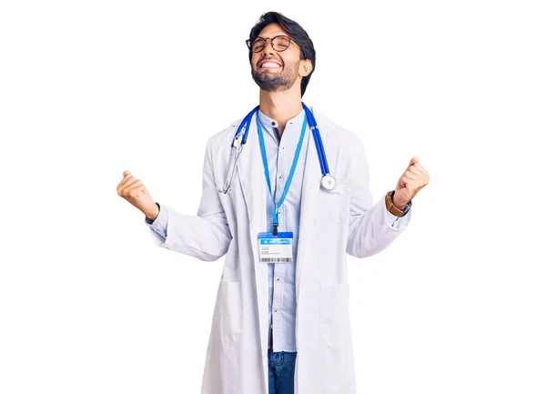 医師の制服を着たハンサムなヒスパニック系の男と聴診器は非常に満足し 腕を上げて勝者のジェスチャーを行う興奮 笑顔と成功のために叫んで お祝いのコンセプト — ストック写真