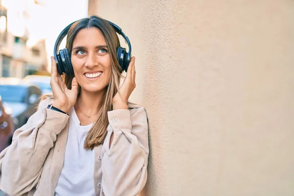 在城市里 年轻的高加索女人用耳机高兴地听着音乐 — 图库照片