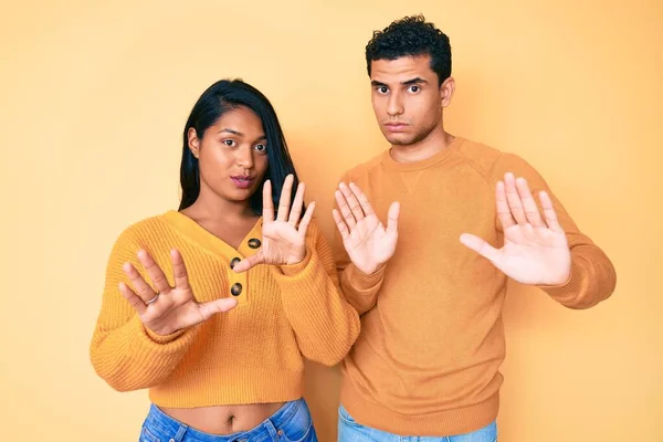 美しいラテン系の若いカップル一緒に手の手のひらを離れて移動カジュアルな服を着て恐怖と嫌な表情で拒否と否定を示しています 止めて禁止する — ストック写真