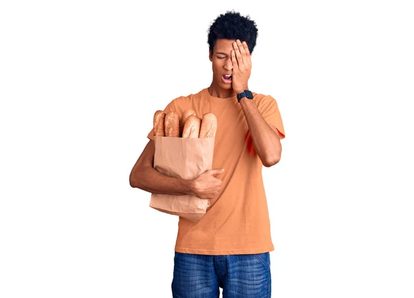若いアフリカ系アメリカ人の男性がパンを手で半分の顔 目と口をカバー疲れてあくびをして紙袋を保持 痛みで顔が痛い — ストック写真