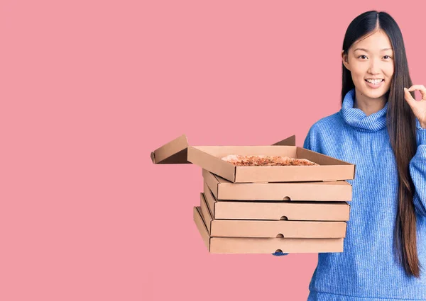 年轻美丽的中国女人拿着一盒纸盒意大利披萨 手拿着手签 微笑着表示友善的手势 象征着极好的象征 — 图库照片