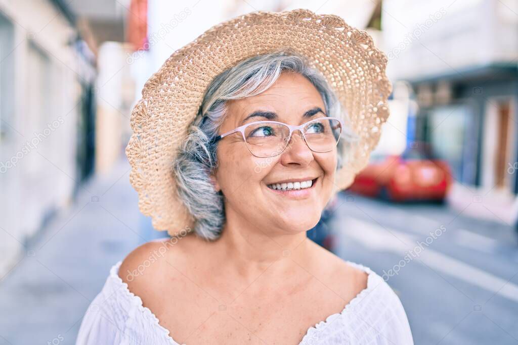 Middle age woman with grey hair smiling happy wearing summer hat outdoors