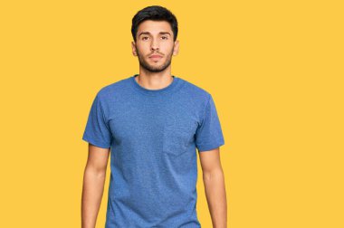 Yüzünde ciddi bir ifade olan sıradan kıyafetler giyen genç yakışıklı bir adam. Basit ve doğal bir şekilde kameraya bakıyorsun.. 