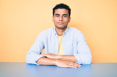 Genç, yakışıklı, günlük kıyafetler giyen, yüzünde ciddi bir ifadeyle masada oturan İspanyol bir adam. Basit ve doğal bir şekilde kameraya bakıyorsun.. 