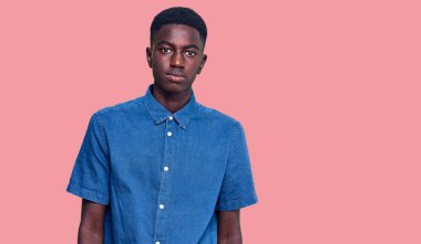 Gündelik kıyafetler giyen genç Afro-Amerikan adam yüzünde ciddi bir ifadeyle rahatlamış. Basit ve doğal bir şekilde kameraya bakıyorsun.. 