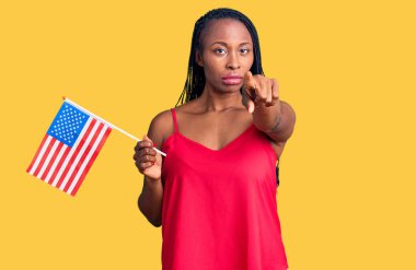 Amerika Birleşik Devletleri bayrağını tutan Afro-Amerikalı genç bir kadın kamerayı işaret ediyor ve sen, kendinden emin bir şekilde ciddi görünüyorsun. 