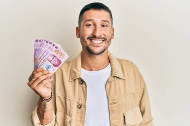 Dövmeleri olan yakışıklı bir adam 50 Meksika pezosu tutuyor. Olumlu ve mutlu görünüyor. Kendine güvenen bir gülümsemeyle dişlerini gösteriyor. 