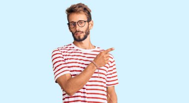 Sakallı, sıradan giyinen ve gözlüklü yakışıklı bir adam. El parmağı yanda, ciddi ve sakin bir yüz ifadesi var. 