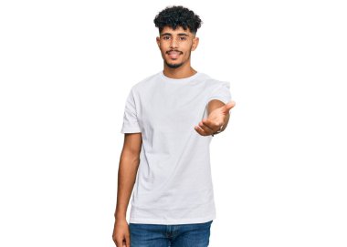 Gündelik beyaz tişört giyen genç Arap adam gülümsüyor. Avuç içi dolusu yardım eli uzatıyor ve kabul ediyor.. 