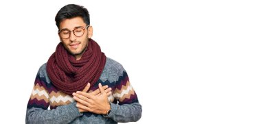 Kış süveteri giyen, elleri göğsünde, gözleri kapalı gülümseyen ve yüzünde minnet ifadesi olan genç yakışıklı bir adam. sağlık kavramı. 