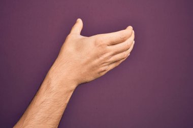 Kafkas 'lı genç adam parmaklarını mor arkaplanda gösteriyor. Elinde görünmez bir nesne var. Elleri boş, kırpma hareketi yapıyor.