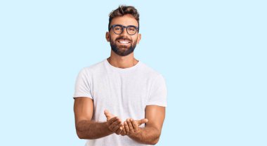 Elleri avuçlarında gülümseyen, günlük kıyafetler ve gözlük takan İspanyol genç bir adam el hareketi yapıyor. Bekleme ve koruma 