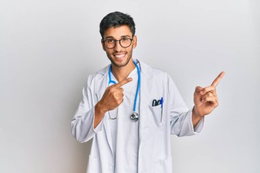 Doktor üniforması giyen, steteskop takan, gülümseyen ve kameraya bakan genç yakışıklı bir adam.. 