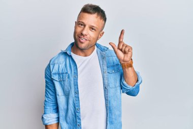 Yakışıklı, sıradan kot ceket giyen kaslı bir adam bir numaralı parmağını gösterip gösterirken kendine güvenen ve mutlu bir şekilde gülümsüyor.. 