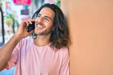 Genç İspanyol adam gülümsüyor. Akıllı telefonda konuşuyor. Duvara yaslanıyor.