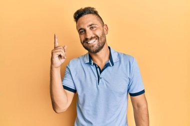 Sakallı, sıradan kıyafetler giyen yakışıklı bir numaralı parmağı gösterip işaret eden, kendinden emin ve mutlu gülümseyen adam.. 